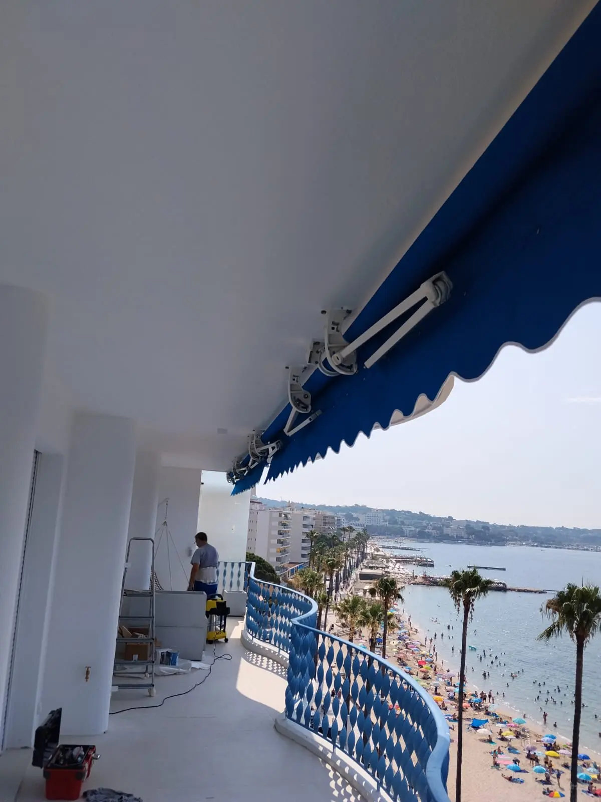 Store banne bleu sur un balcon avec vue sur la plage et la mer.