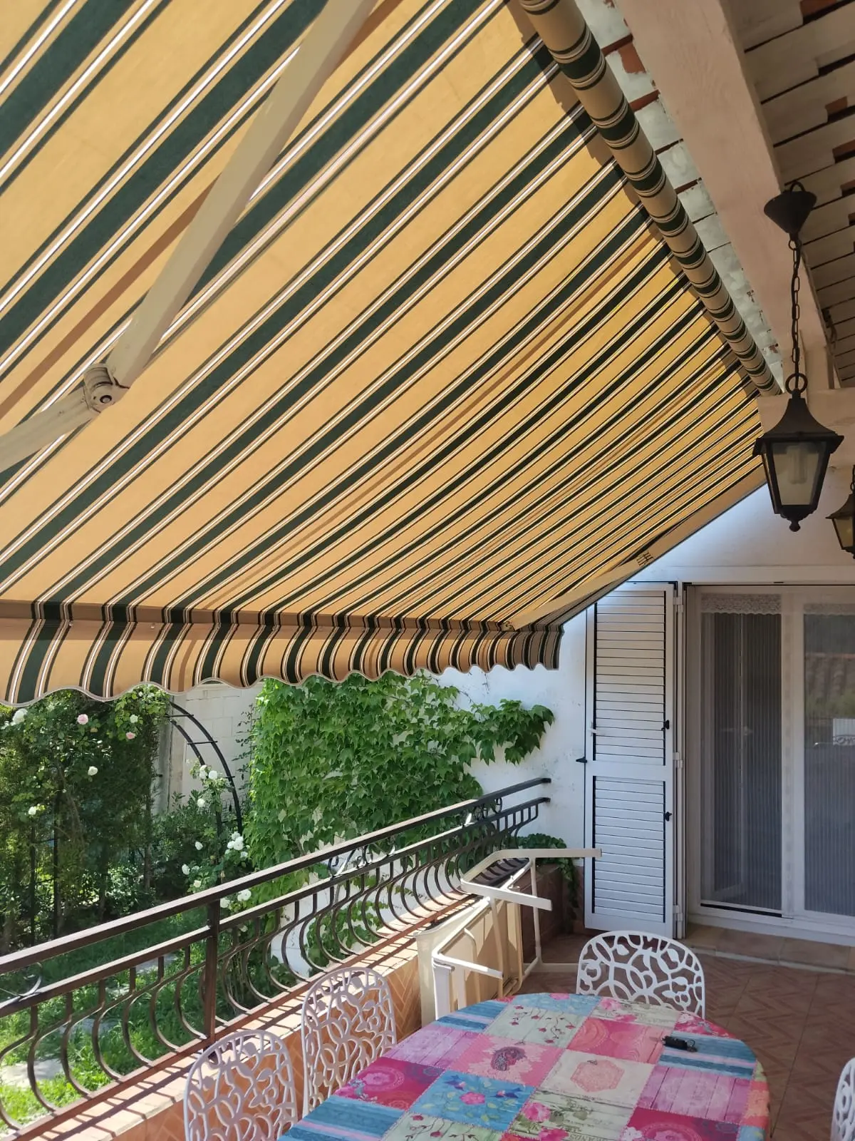 Store banne à rayures vertes et beiges protégeant une terrasse aménagée.